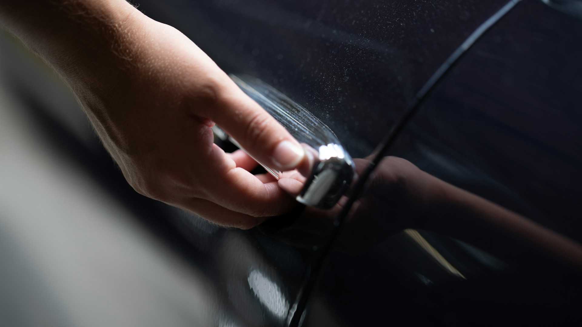 Mão na maçaneta de um carro escuro: na retirada por autoatendimento, a locadora não vê quem abre o veículo. Foto: Rapha Wilde, Unsplash